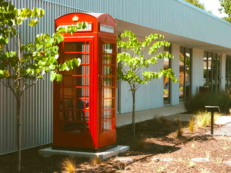 A red telephone box on the lawn at The Front Porch, beside the building with young trees and planting around it